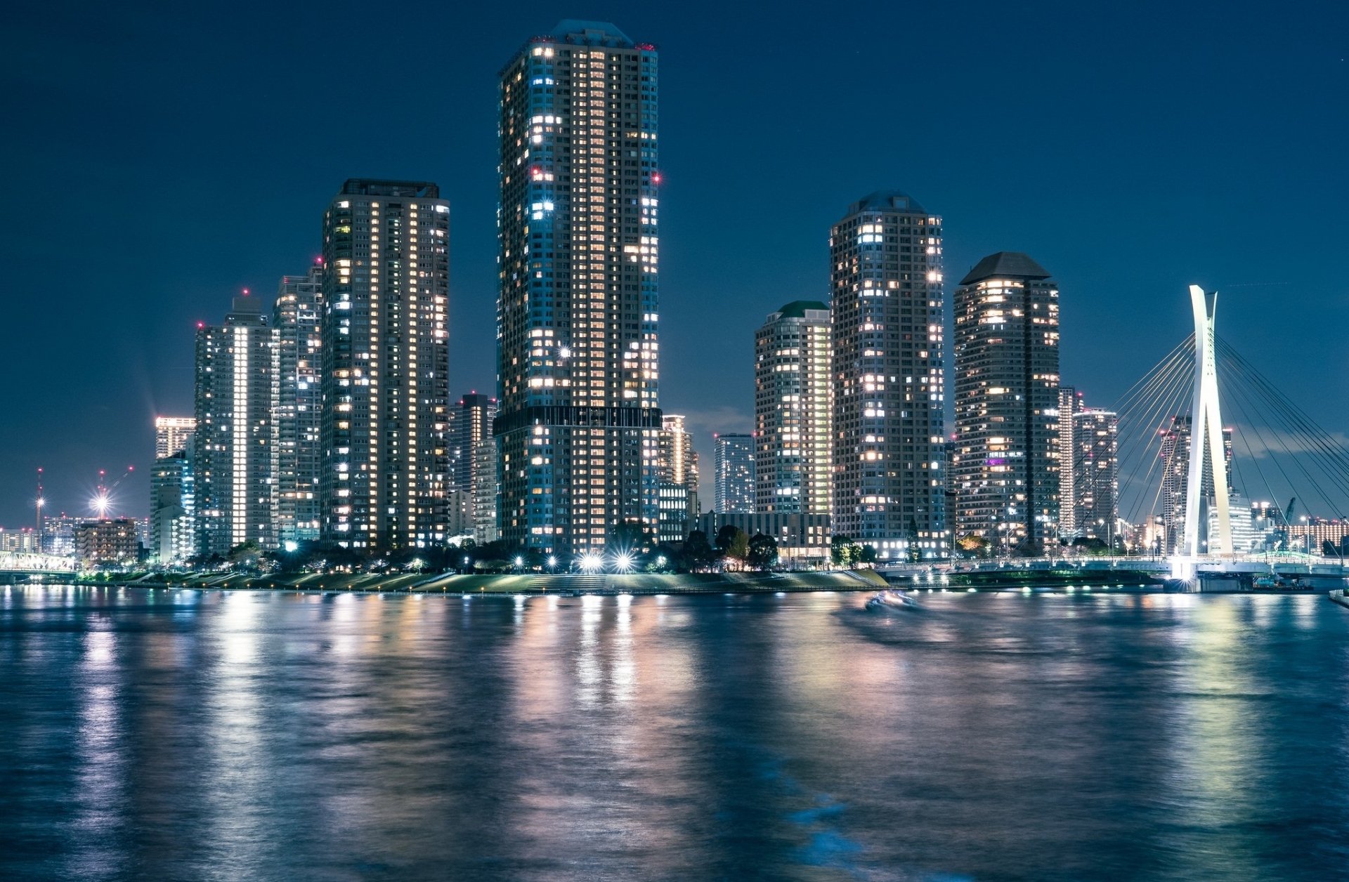 HD desktop wallpaper showcasing a man-made Tokyo skyline at night with illuminated skyscrapers reflected on calm water.