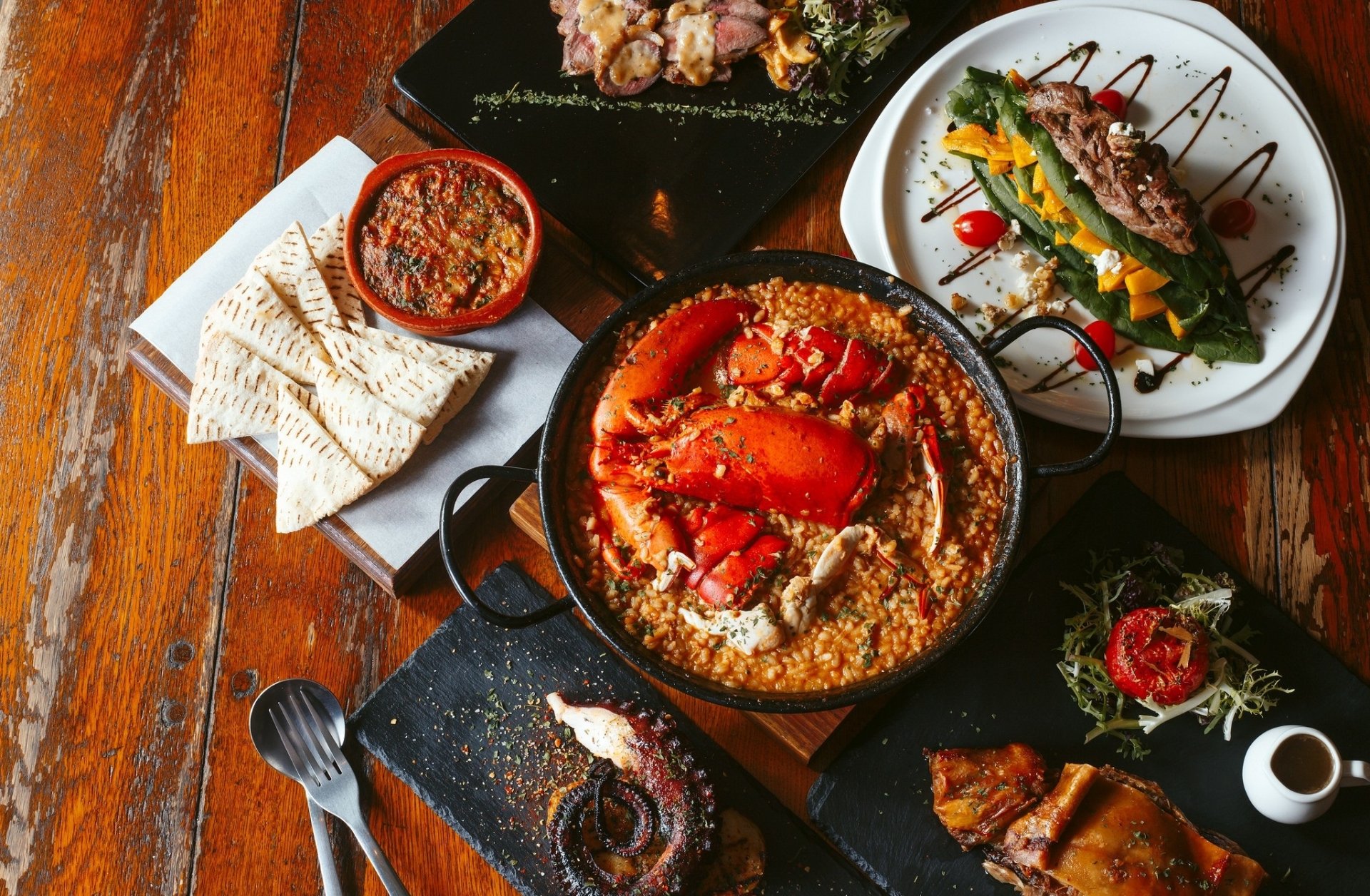 HD PC desktop wallpaper of Japanese food: vibrant seafood and small plates on a wooden table, grilled and garnished dishes arranged around a central seafood rice pot.