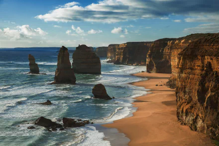 HD desktop wallpaper showcasing the stunning cliffs and beach of The Twelve Apostles, a natural landmark along Australia's coastline under a partly cloudy sky.