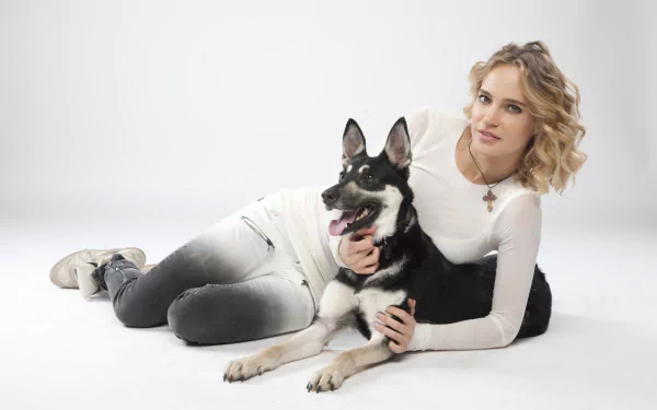 Blonde Russian pop singer reclining with her dog on a white studio background — 5K Ultra HD desktop wallpaper.
