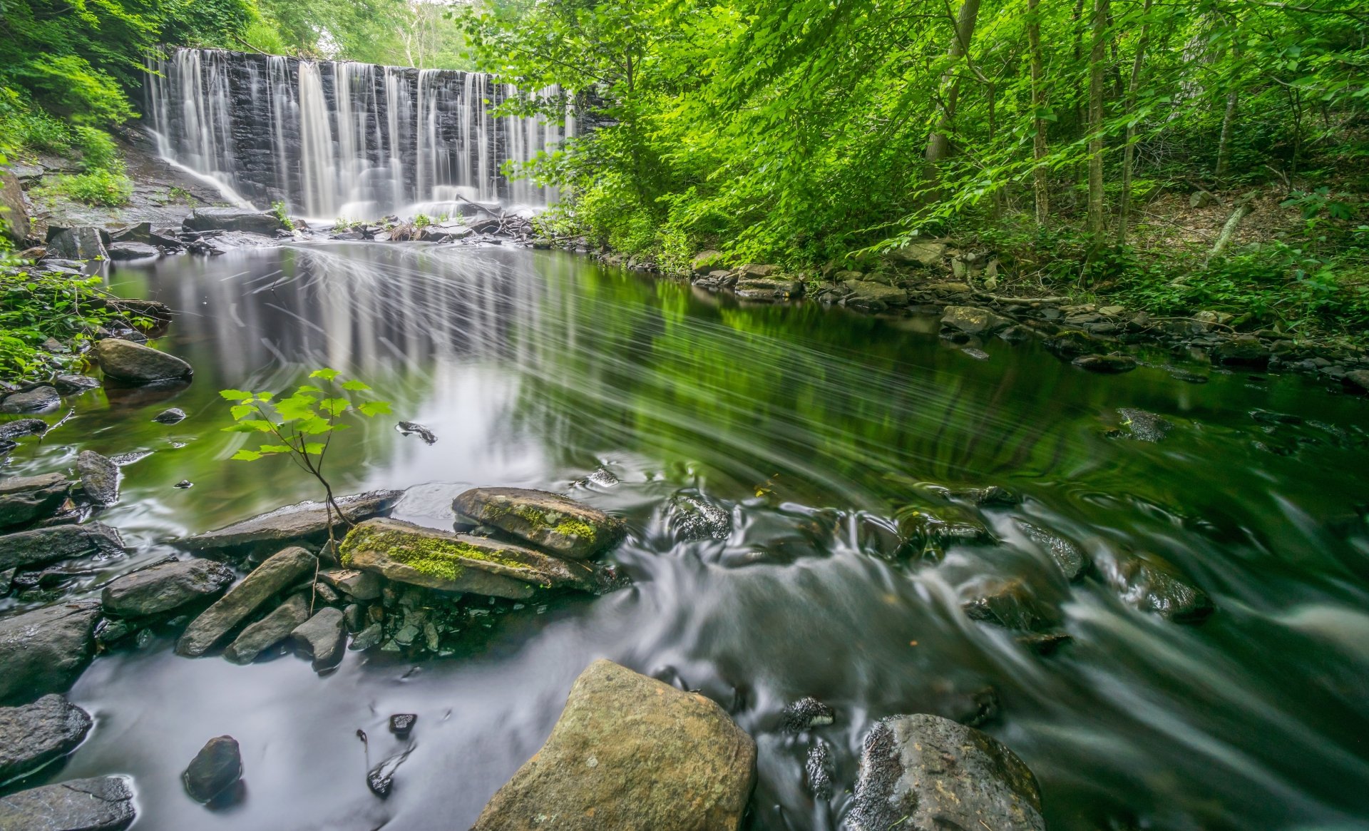 4K Ultra HD wallpaper of a serene waterfall flowing over stone ledges into a clear river, surrounded by lush green trees in a Connecticut nature setting.