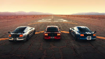 Three Ford Shelby GT500 cars, including a silver one, are lined up on a cracked runway at sunset in this 4K Ultra HD desktop wallpaper.
