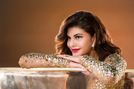 A smiling Jacqueline Fernandez, Sri Lankan actress and model with brunette hair and brown eyes, rests on a glittery surface in this HD desktop wallpaper. She wears red lipstick and a sparkling outfit.