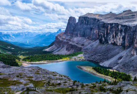 Stunning HD wallpaper of Banff National Park featuring a clear lake surrounded by lush greenery and rocky mountains under a partly cloudy sky.