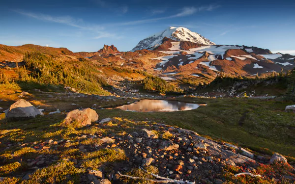 4K Ultra HD desktop wallpaper showcasing Mount Rainier with rugged mountain terrain, vibrant greenery, and a clear blue sky in a stunning natural landscape.