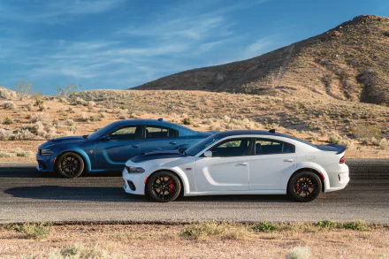 Two Dodge Charger SRT muscle cars, including a white Dodge Charger SRT Hellcat, parked side by side on a desert road under a blue sky, HD desktop wallpaper.