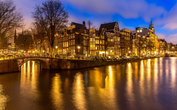 Night view of Amsterdam’s illuminated canal and historic buildings reflecting on the water, showcasing the man-made cityscape of the Netherlands in 4K Ultra HD.