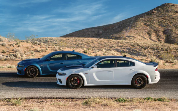 Two Dodge Charger SRT muscle cars, including a white Dodge Charger SRT Hellcat, parked side by side on a desert road under a blue sky, HD desktop wallpaper.