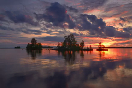 HD desktop wallpaper of a Finnish lake at sunset, featuring trees on small islands and dramatic clouds reflecting on the calm water, showcasing serene nature.
