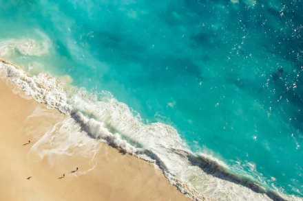 Aerial HD desktop wallpaper showing a blue coastline with waves gently crashing onto a sandy beach.