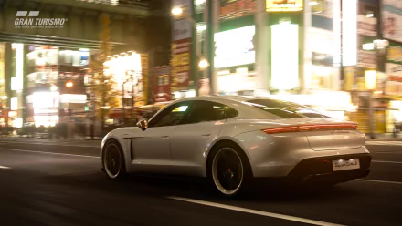HD desktop wallpaper featuring a white Porsche Taycan Turbo S driving through a brightly lit city street at night, tagged with Porsche and video game Gran Turismo Sport.
