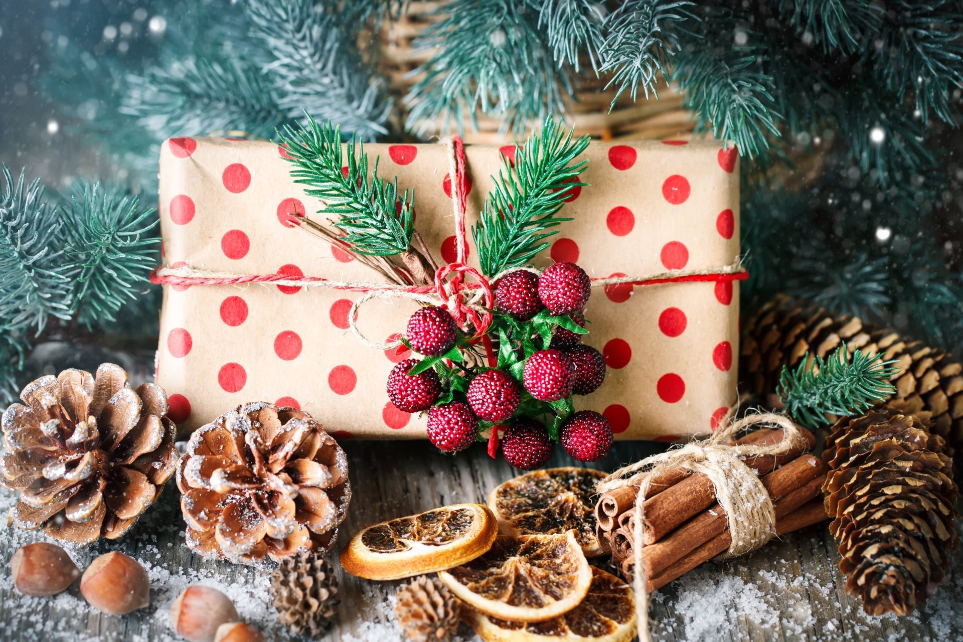 4K Ultra HD PC desktop wallpaper: polka-dot wrapped gift topped with an evergreen sprig and berries, surrounded by pine cones, cinnamon sticks and dried orange slices dusted with snow.
