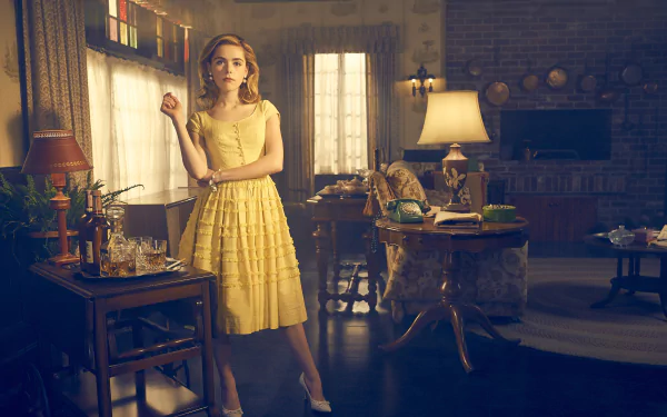 Kiernan Shipka from the TV show Feud stands in a vintage-style room wearing a yellow dress, captured in a high-definition desktop wallpaper scene.