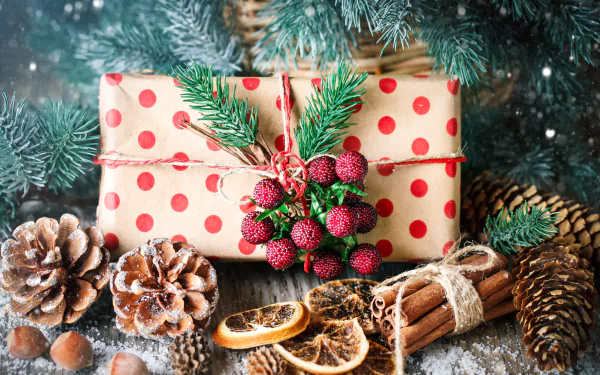 4K Ultra HD PC desktop wallpaper: polka-dot wrapped gift topped with an evergreen sprig and berries, surrounded by pine cones, cinnamon sticks and dried orange slices dusted with snow.