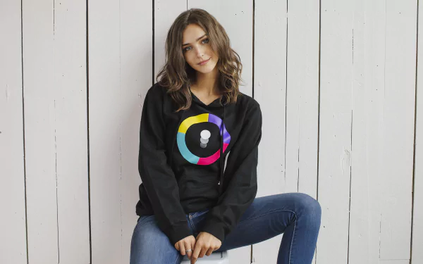 HD desktop wallpaper featuring Rachel Cook, an American brunette model, seated casually against a white wooden backdrop.