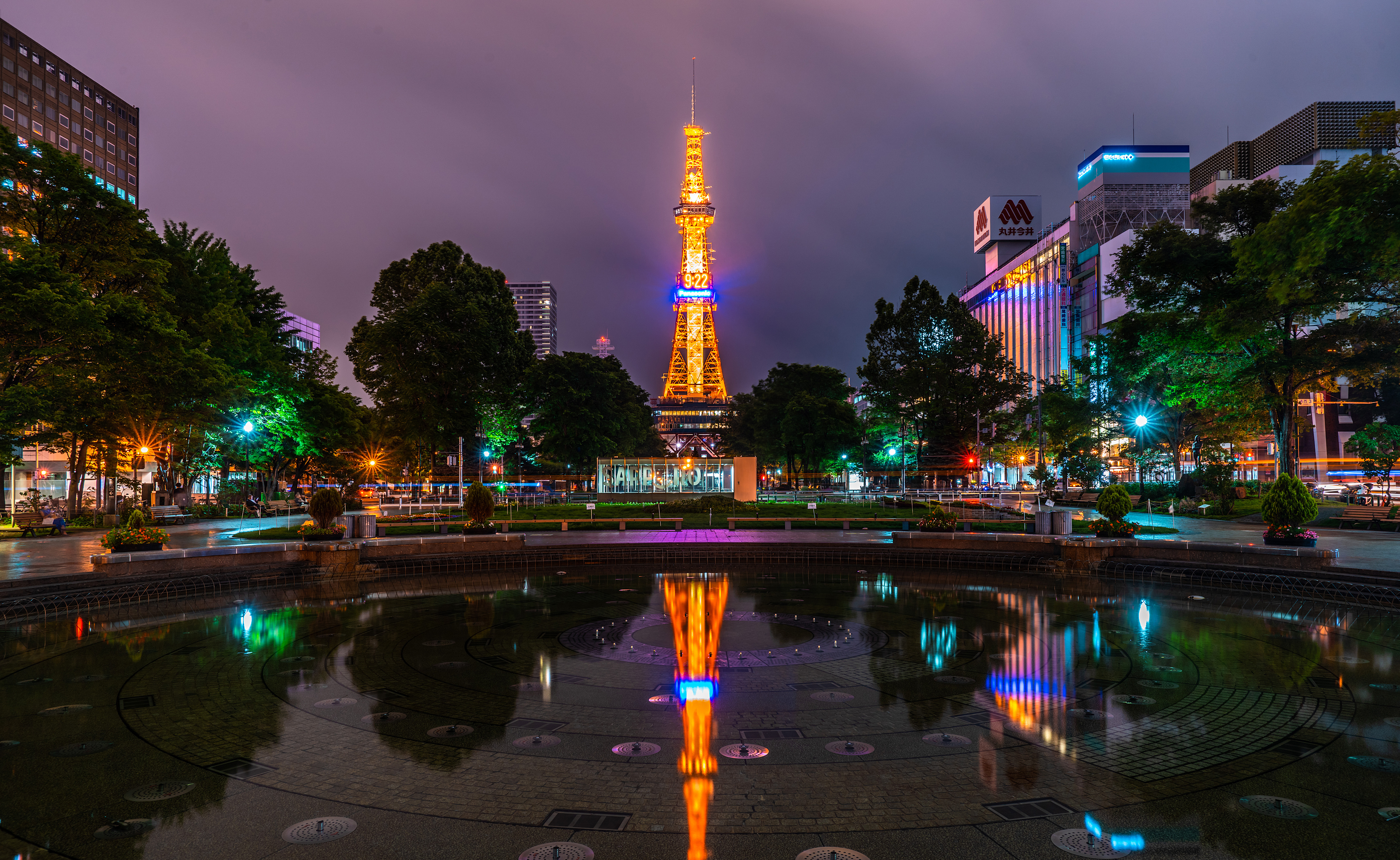 A stunning night view of Sapporo, Japan, showcasing a tower and city buildings illuminated by vibrant lights, creating a captivating reflection.