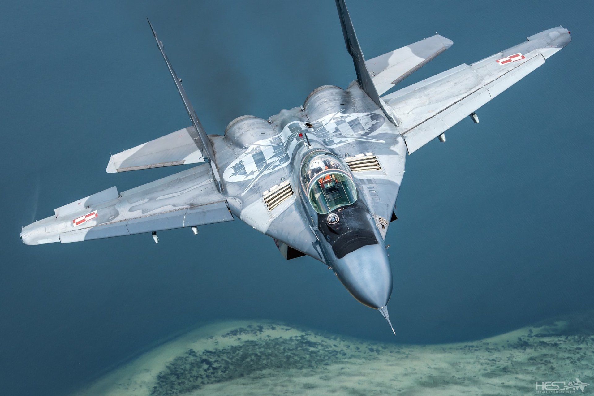 HD PC desktop wallpaper of a Mikoyan MiG-29 military jet fighter warplane in flight over coastline, forward view of the gray aircraft and cockpit.