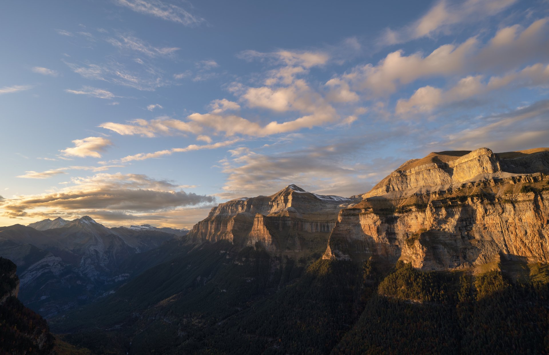 5K Ultra HD PC desktop wallpaper: sunlit limestone cliffs and deep green nature valley of Ordesa Valley, Spain, beneath a wide sky scattered with clouds.
