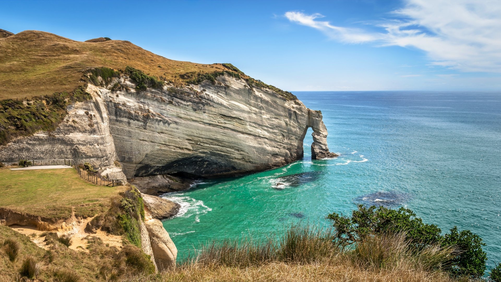 4K Ultra HD image of a coastal arch formation on the New Zealand coastline, featuring clear turquoise waters and rugged natural cliffs under a blue sky.