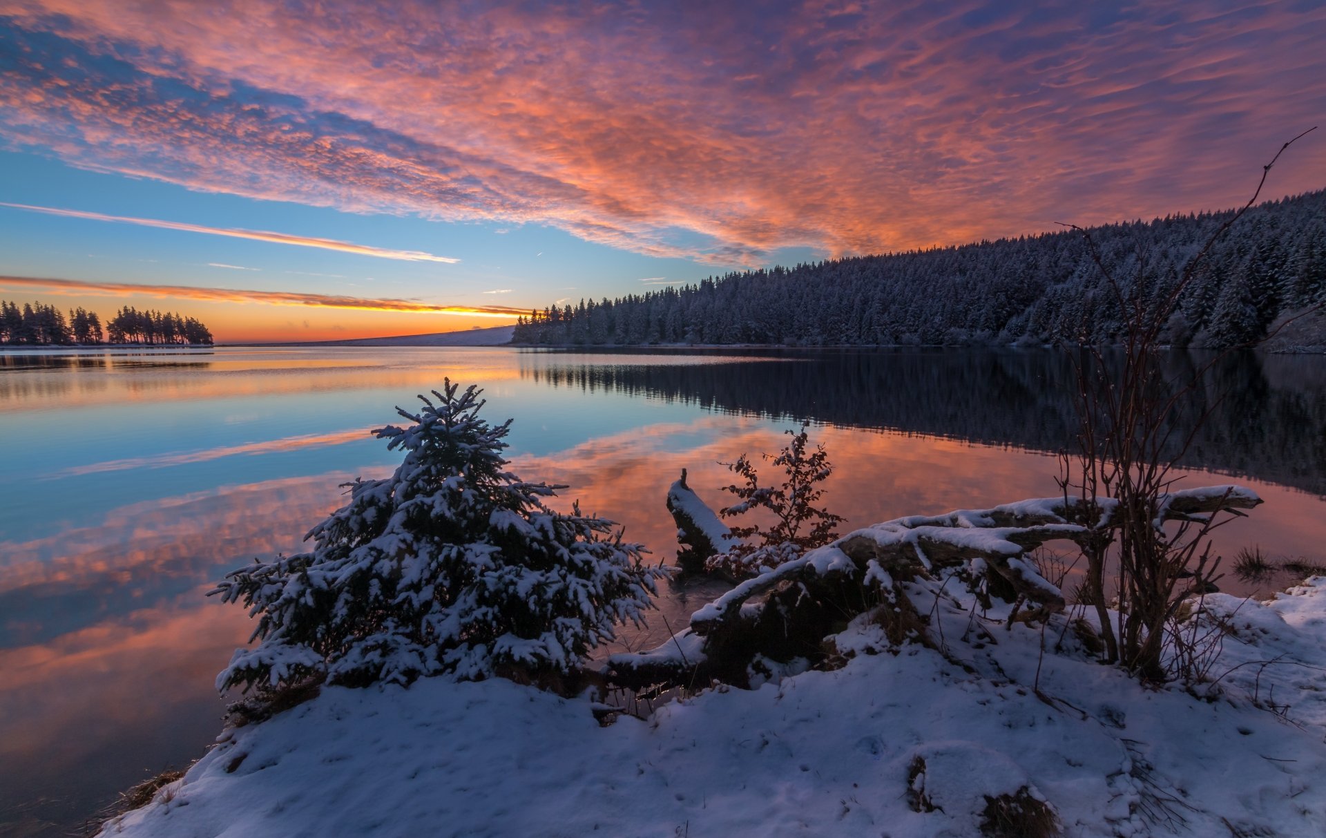 Snow-covered shore and trees reflect vibrant dawn clouds over a tranquil winter lake, captured in stunning 4K Ultra HD for a serene nature desktop wallpaper.