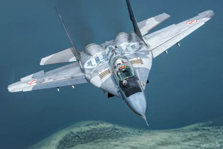 HD PC desktop wallpaper of a Mikoyan MiG-29 military jet fighter warplane in flight over coastline, forward view of the gray aircraft and cockpit.