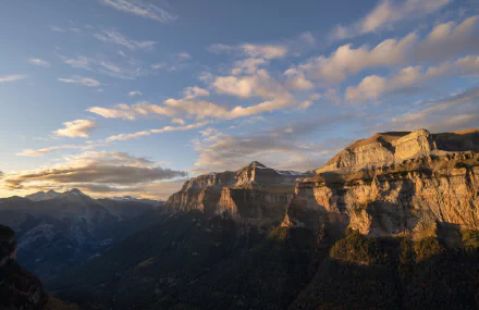 5K Ultra HD PC desktop wallpaper: sunlit limestone cliffs and deep green nature valley of Ordesa Valley, Spain, beneath a wide sky scattered with clouds.