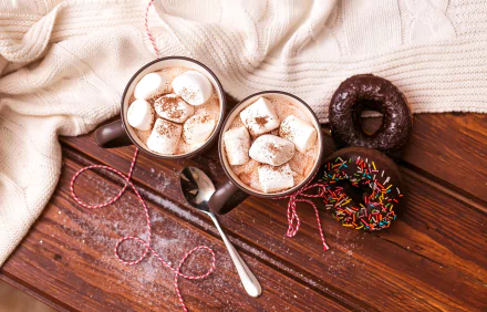 Still life HD desktop wallpaper featuring two cups of hot chocolate topped with marshmallows, accompanied by two doughnuts, on a wooden surface with a cozy knit blanket.