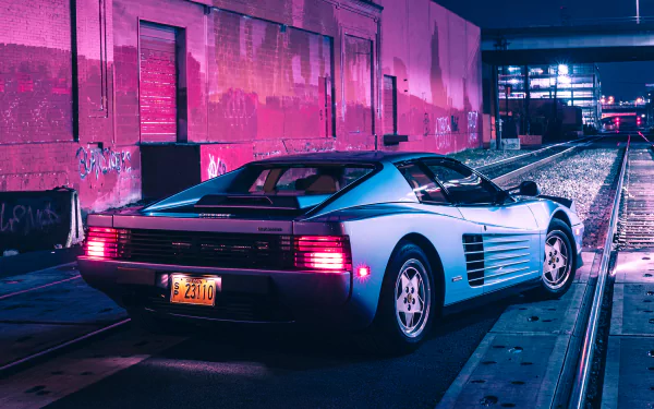 Rear three-quarter view of a silver Ferrari Testarossa parked on rail tracks in a neon magenta-lit industrial alley at night — 2K Quad HD PC desktop wallpaper.