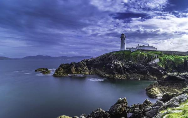 4K Ultra HD image of a man-made lighthouse on a rocky Irish coast under dramatic clouds and a vibrant sky.
