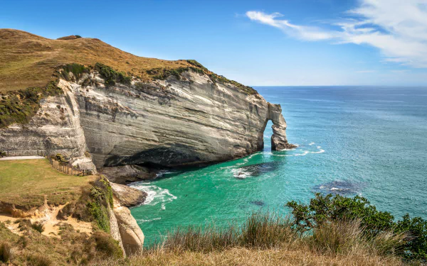 4K Ultra HD image of a coastal arch formation on the New Zealand coastline, featuring clear turquoise waters and rugged natural cliffs under a blue sky.