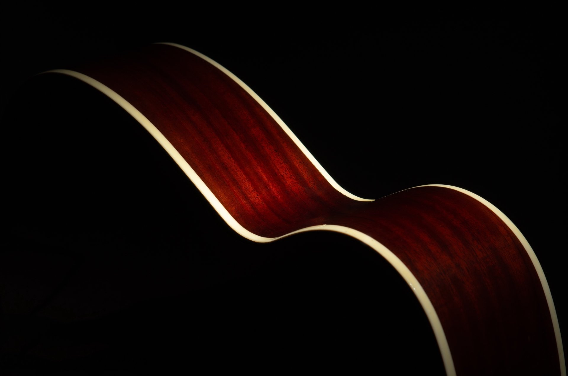 Close-up of a glossy acoustic guitar's curved mahogany body against deep black — 4K Ultra HD PC desktop wallpaper and background conveying music mood.