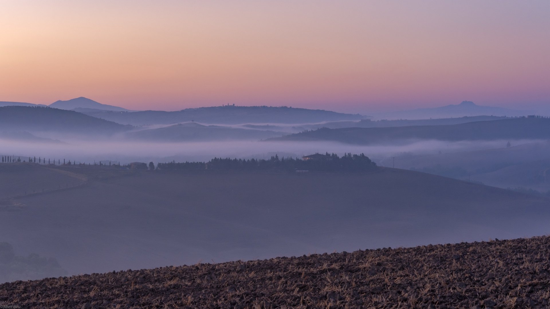 Foggy Tuscan landscape at dawn with layered hills under a pastel sky, captured in stunning 4K Ultra HD photography.