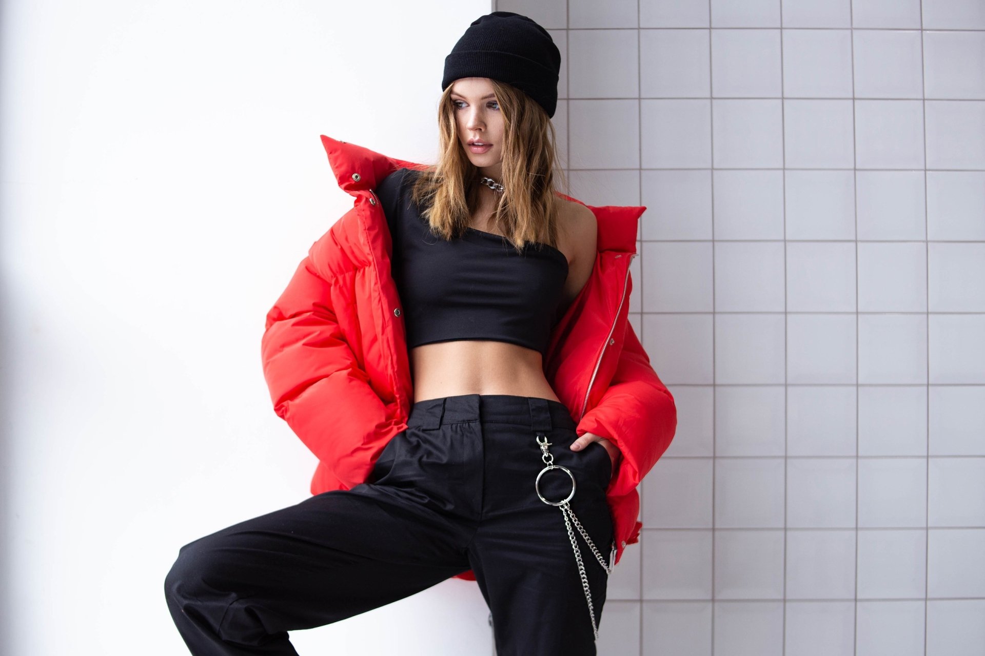 HD PC desktop wallpaper of a woman wearing a red puffer jacket, black crop top, and black pants, posing confidently against a tiled white wall.