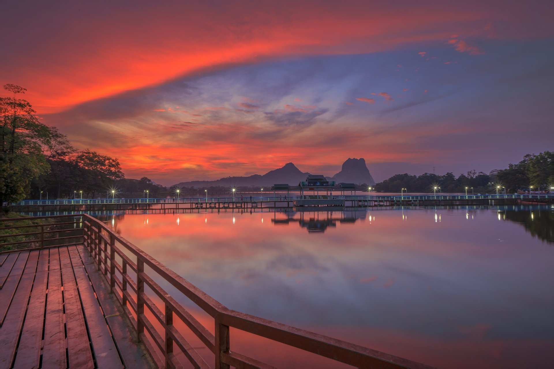 HD PC desktop wallpaper: sunset lake photography with dramatic clouds, a wooden pier in the foreground and silhouetted hills reflected in calm water.