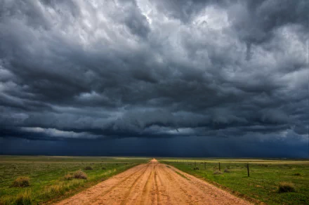 4K Ultra HD desktop wallpaper depicting a dirt road under a dramatic stormy sky with dark clouds stretching over an open natural landscape.