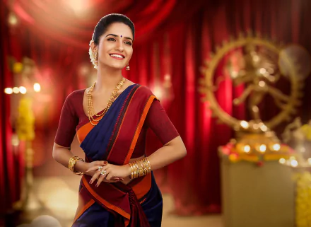 Bollywood actress Ruhani Sharma in a vibrant saree with gold jewelry and lipstick, smiling warmly against a rich red background with artistic depth of field.
