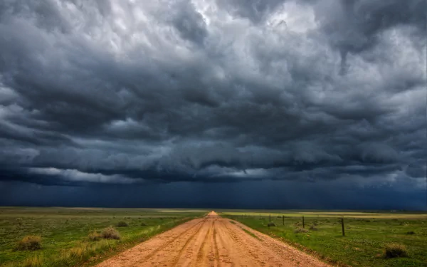 4K Ultra HD desktop wallpaper depicting a dirt road under a dramatic stormy sky with dark clouds stretching over an open natural landscape.