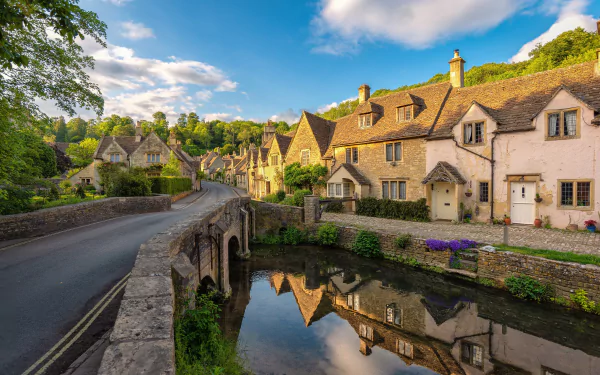 4K UHD desktop wallpaper of a Cotswolds village in Wiltshire, England: man-made stone bridge spanning a river, honey-coloured cottages and their reflections under a blue sky.