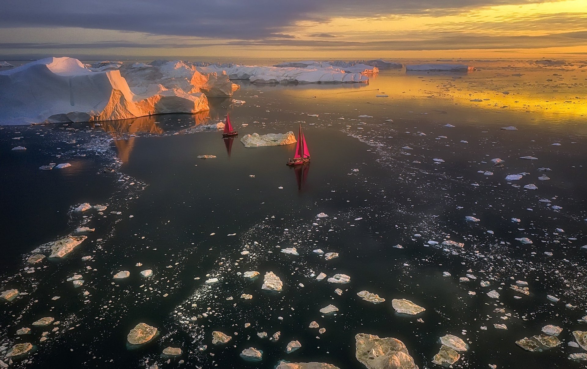 HD landscape photography of boats sailing through icy waters near towering icebergs in Greenland at sunset, with a serene ocean and scattered ice floes.