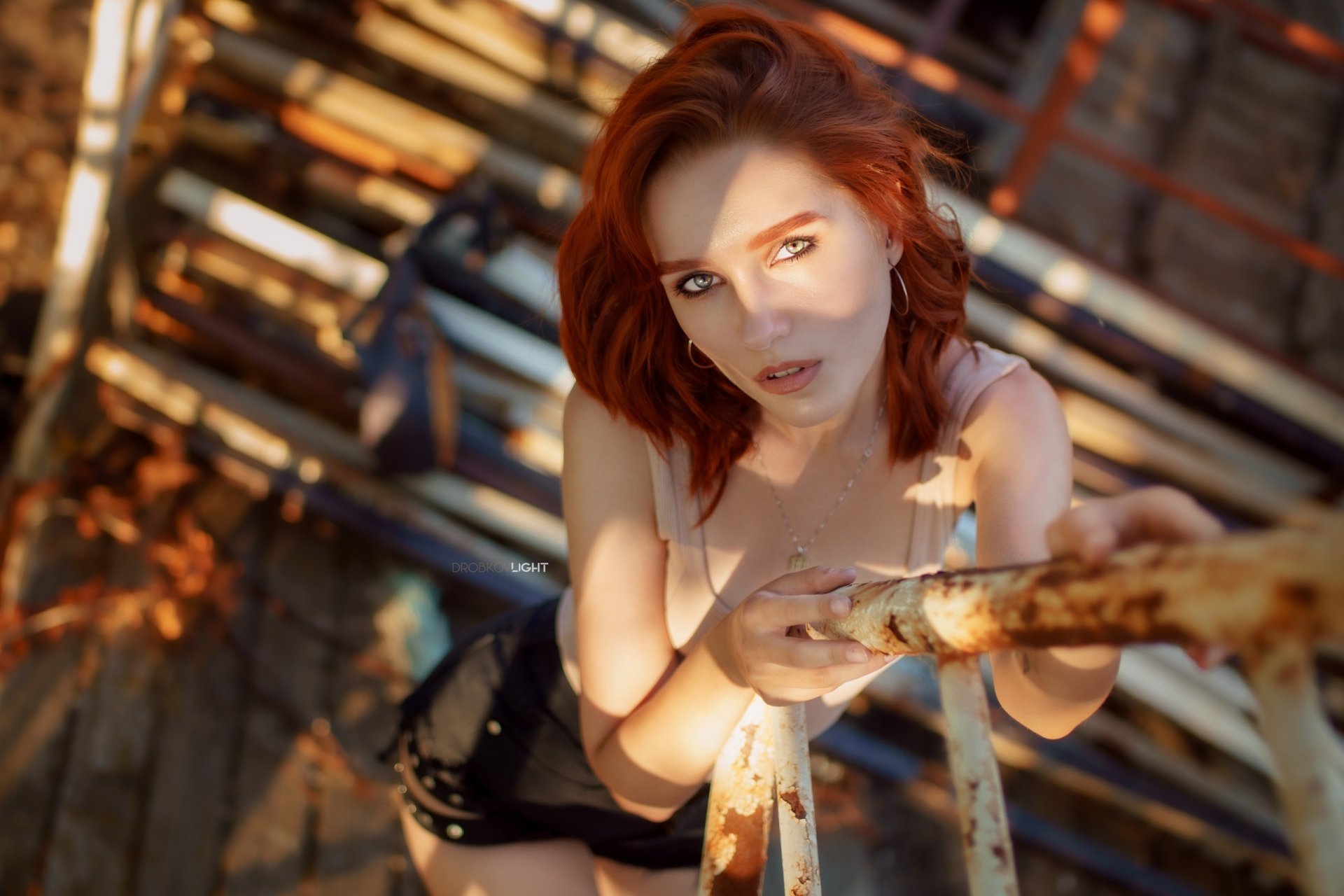 HD desktop wallpaper featuring redhead model Maria Larina looking up through sunlit metal scaffolding with warm shadows and urban textures.