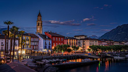 4K Ultra HD desktop wallpaper of Ascona, Switzerland — colorful man-made harbor at dusk, waterfront houses and church tower, moored boats with mountains in the background.