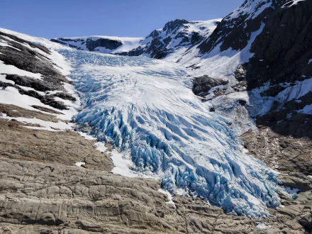 8K Ultra HD wallpaper showcasing a vast glacier flowing between rocky mountains under a clear blue sky, highlighting the raw beauty of ice and nature.
