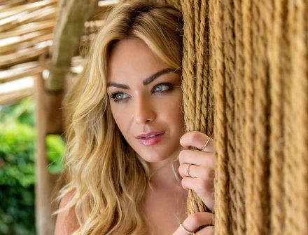 HD PC desktop wallpaper: close-up of a blonde female model's face framed by sunlit hair and thick braided rope, contemplative expression with soft makeup and blurred green foliage behind.