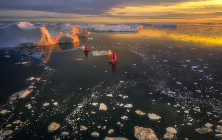 HD landscape photography of boats sailing through icy waters near towering icebergs in Greenland at sunset, with a serene ocean and scattered ice floes.