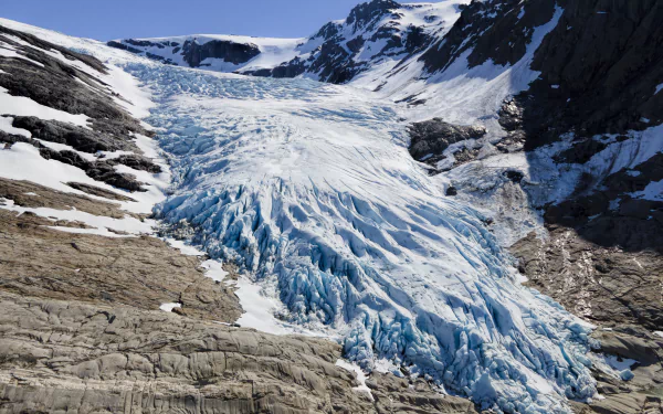 8K Ultra HD wallpaper showcasing a vast glacier flowing between rocky mountains under a clear blue sky, highlighting the raw beauty of ice and nature.