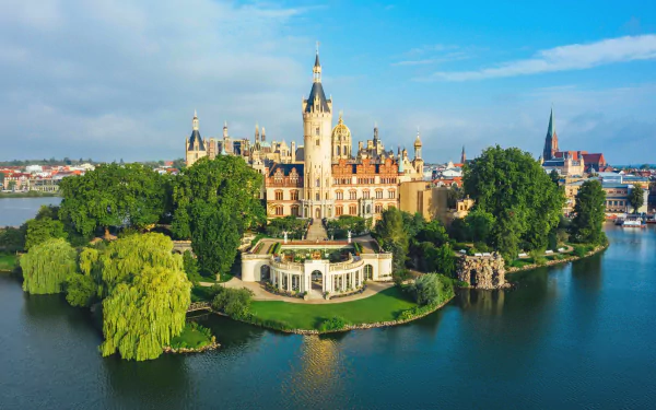 Aerial view of Schwerin Palace, a man-made castle on an island surrounded by a river in Germany, under a bright blue sky.