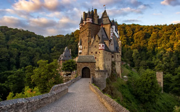 A stunning 4K Ultra HD wallpaper of medieval man-made Eltz Castle nestled among lush green forests under a dramatic sky.