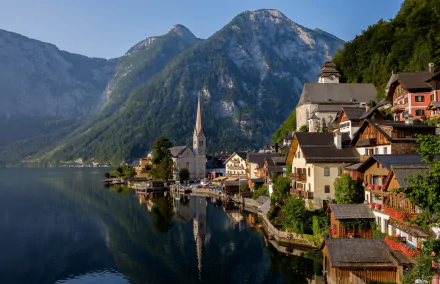 Scenic view of Hallstatt in Austria, featuring man-made lakeside buildings nestled against the Alps mountains under clear skies.