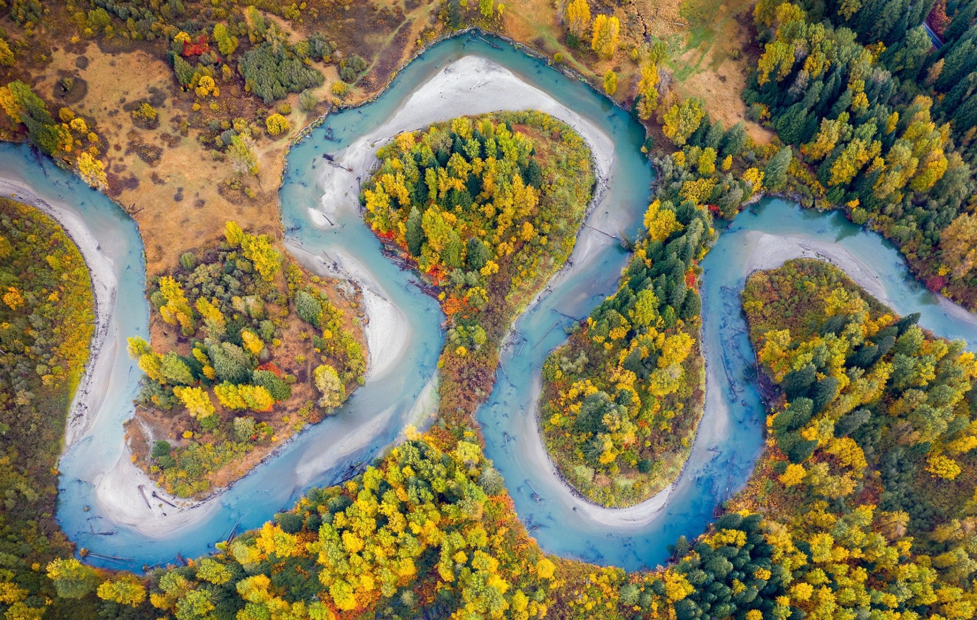Aerial view of a winding river surrounded by vibrant fall foliage in a natural landscape, featured in HD as a desktop wallpaper and background.