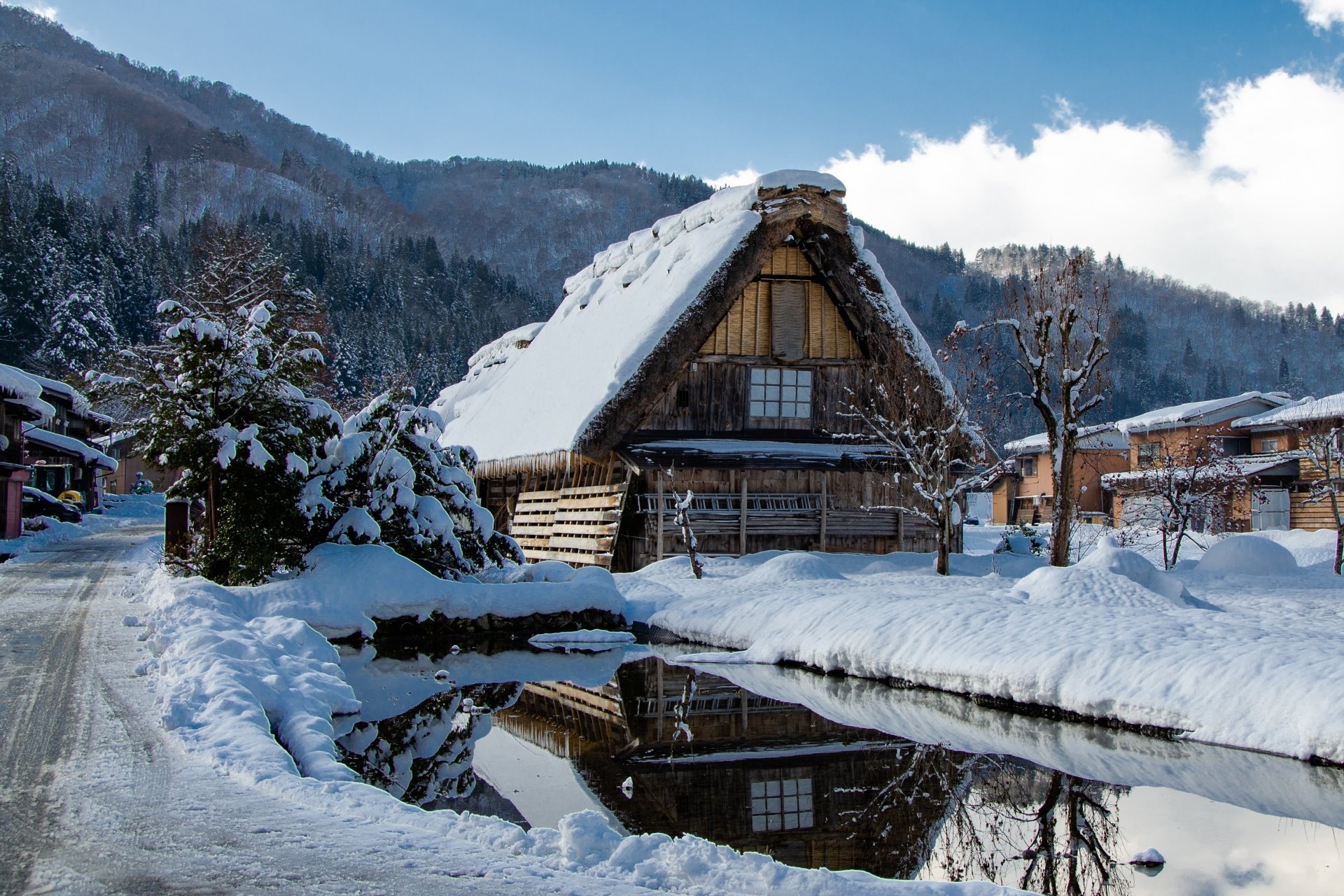 Snow-covered traditional Japanese house in a quiet village surrounded by snowy mountains under a bright winter sky, captured in stunning 4K Ultra HD quality.